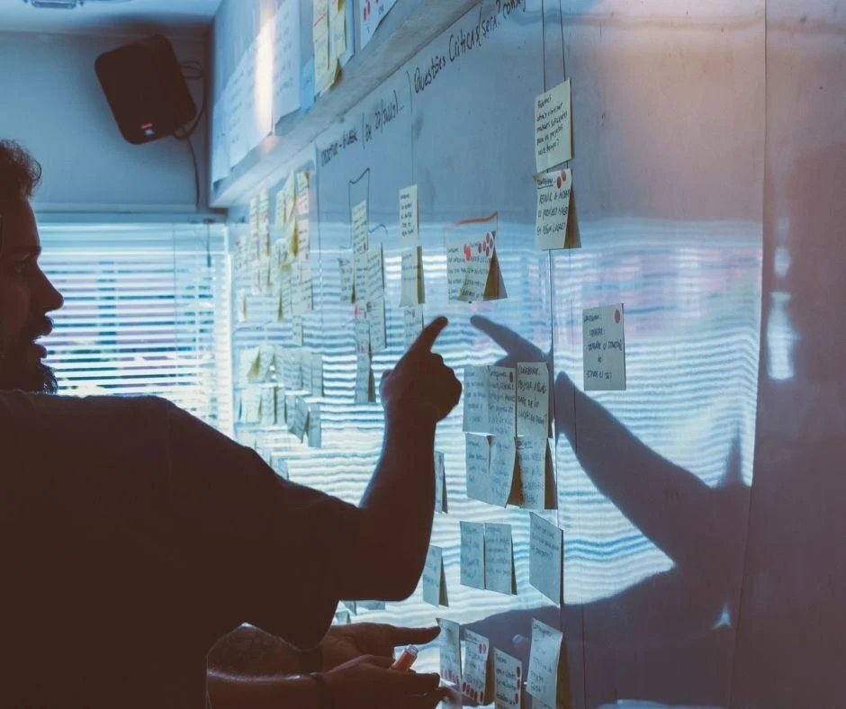 Team member pointing at sticky notes on a glass board while reviewing digital marketing performance strategies