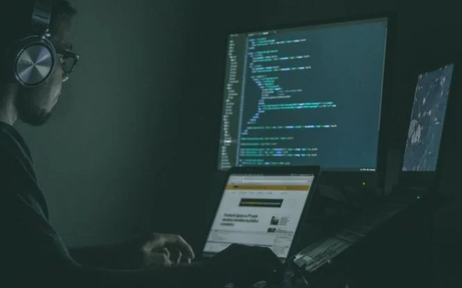 Person wearing headphones working late at night on code, illustrating the hidden tactics behind ad fraud schemes.