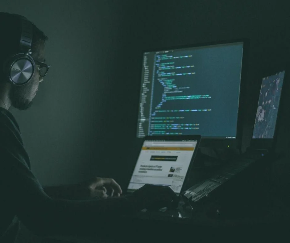 Person wearing headphones working late at night on code, illustrating the hidden tactics behind ad fraud schemes.
