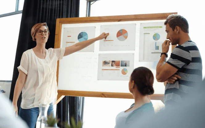Woman presenting data charts on a whiteboard to colleagues, demonstrating an insights driven business approach.