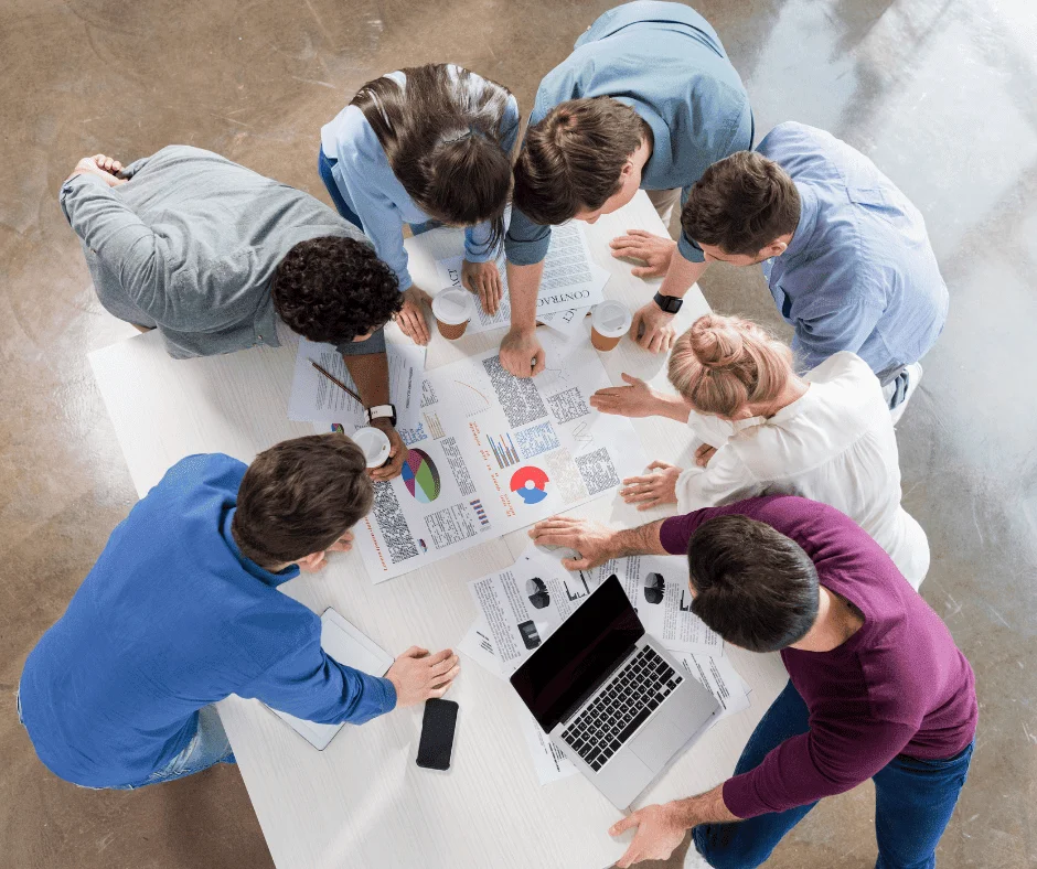 Overhead view of a team reviewing digital marketing reports, charts, and a laptop around a table.
