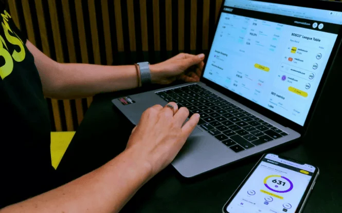 Person analyzing BOSCO dashboard on laptop and phone, showing competitor insights and SEO performance metrics.