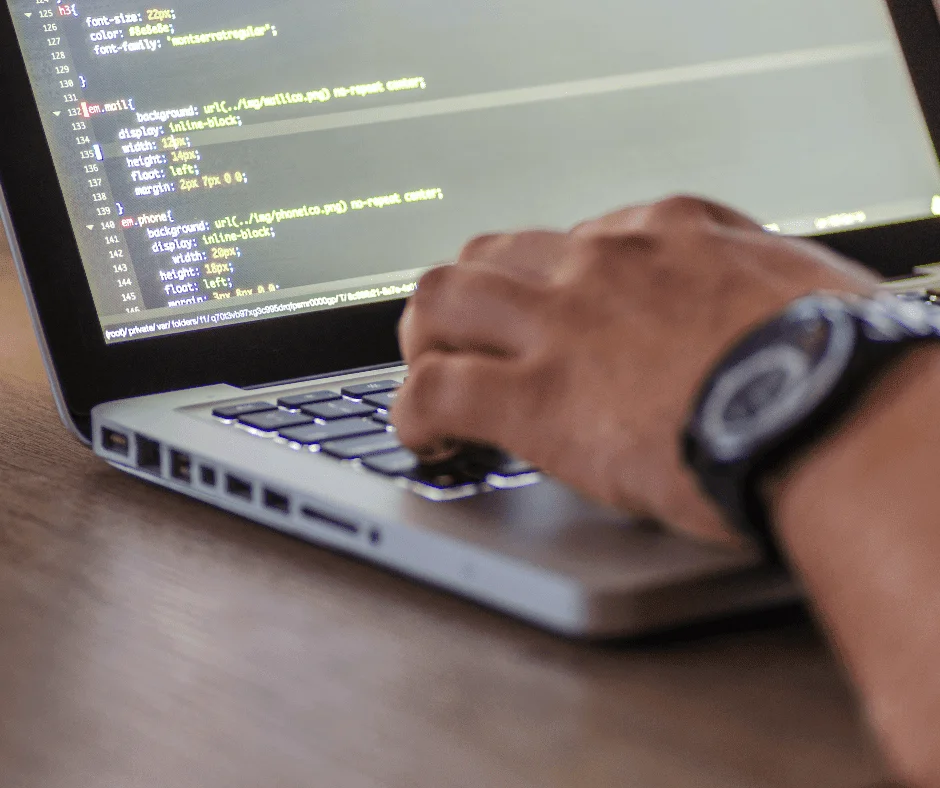 Hand typing CSS code on a laptop keyboard, illustrating the technical setup behind tracking UTM codes.