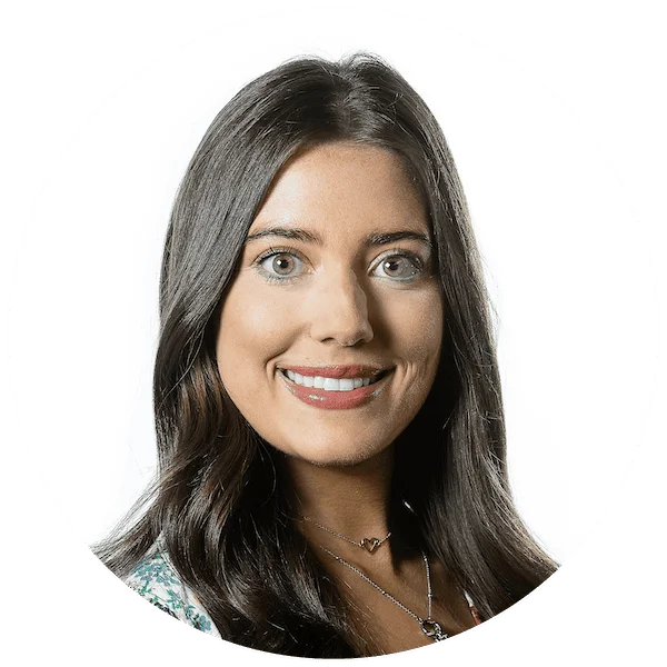 Professional headshot of a smiling woman with long dark hair, wearing a necklace and floral top.