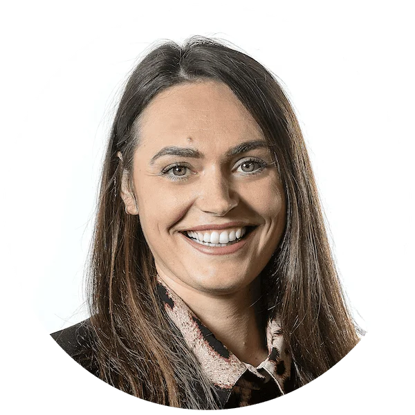 Professional headshot of a smiling woman with long brown hair, wearing a patterned blouse and dark blazer.