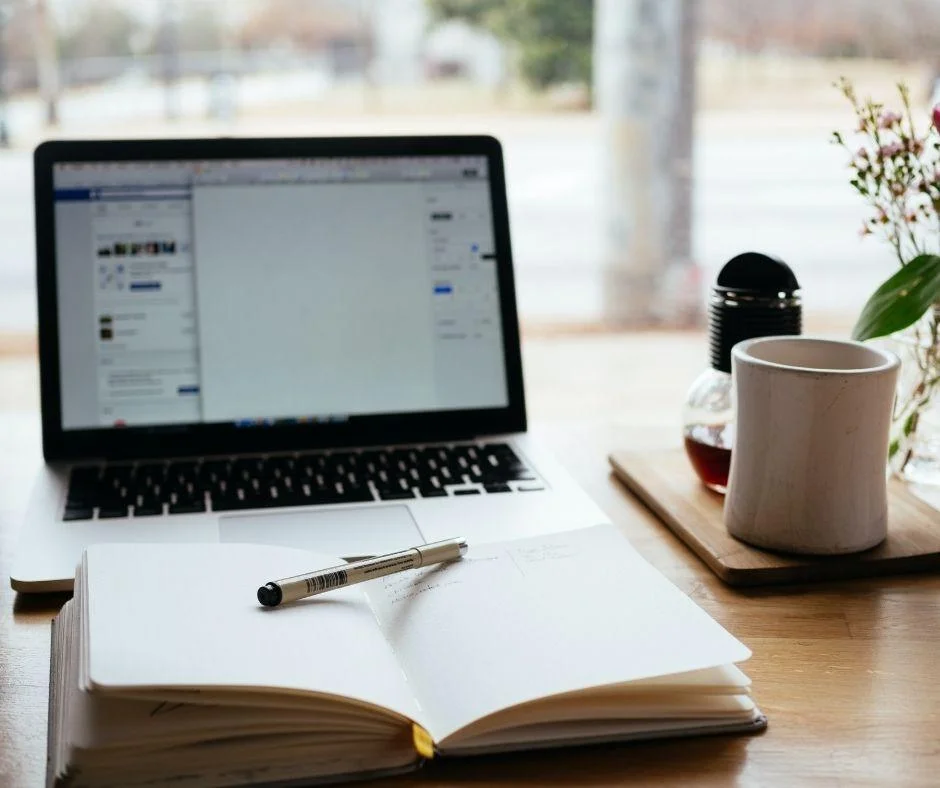 Laptop, open notebook, and coffee mug on a desk, reflecting a daily habit of improving performance.