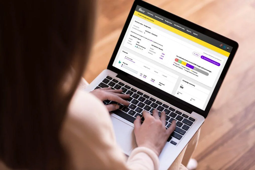 Person viewing a budget plan dashboard in ASK BOSCO® on a laptop, showcasing new data connectors for ad channels.