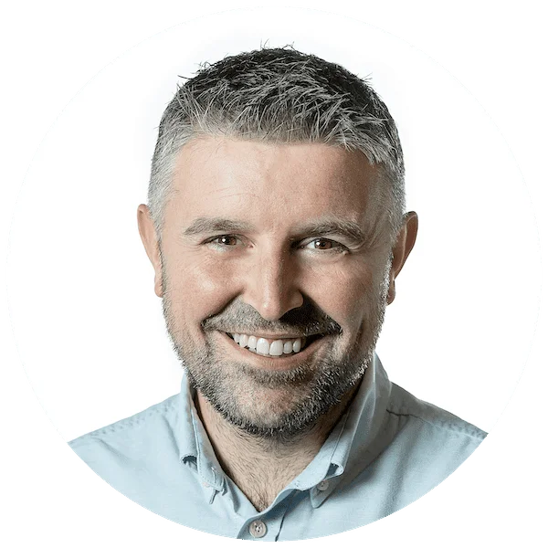 Smiling man with short gray hair and a beard wearing a light blue collared shirt, circular profile photo.