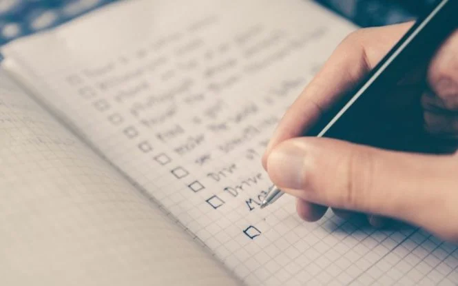Hand writing on an SEO checklist with checkboxes on graph paper using a pen