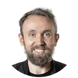 Smiling man with short gray hair and a beard wearing a black shirt, looking slightly upward.