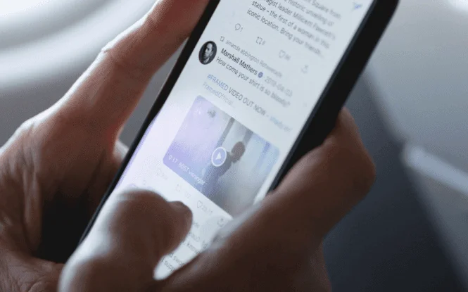 Hands holding a smartphone scrolling a Twitter feed, illustrating discussion around the Twitter blue tick fee.