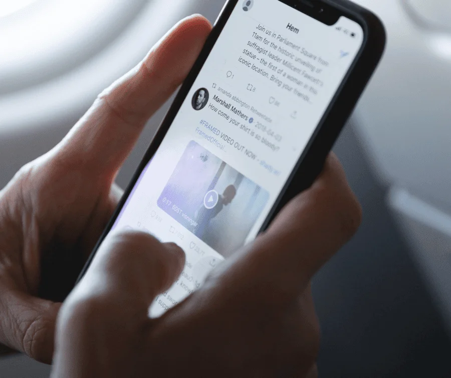 Hands holding a smartphone scrolling a Twitter feed, illustrating discussion around the Twitter blue tick fee.