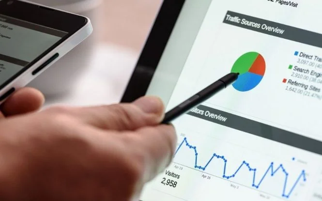 Hand holding a stylus over a tablet displaying website traffic analytics, useful for evaluating PPC ad performance.