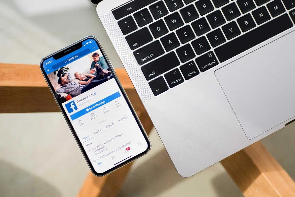Smartphone displaying the Facebook app next to a laptop keyboard, illustrating how to budget for Facebook ads.
