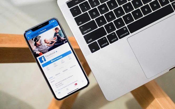 Smartphone displaying the Facebook app next to a laptop keyboard, illustrating how to budget for Facebook ads.