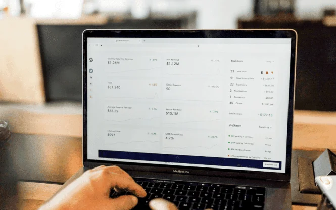 Hands typing on a MacBook Pro displaying a revenue dashboard with MRR, churn, and growth metrics.
