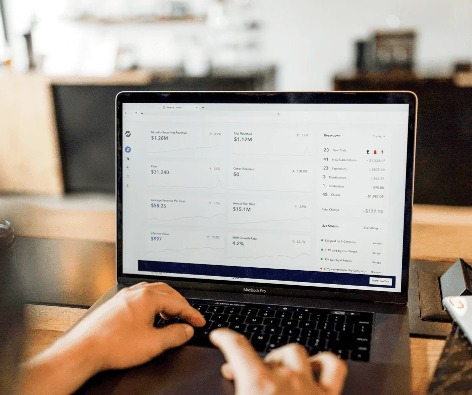 Hands typing on a MacBook Pro displaying a revenue dashboard with MRR, churn, and growth metrics.