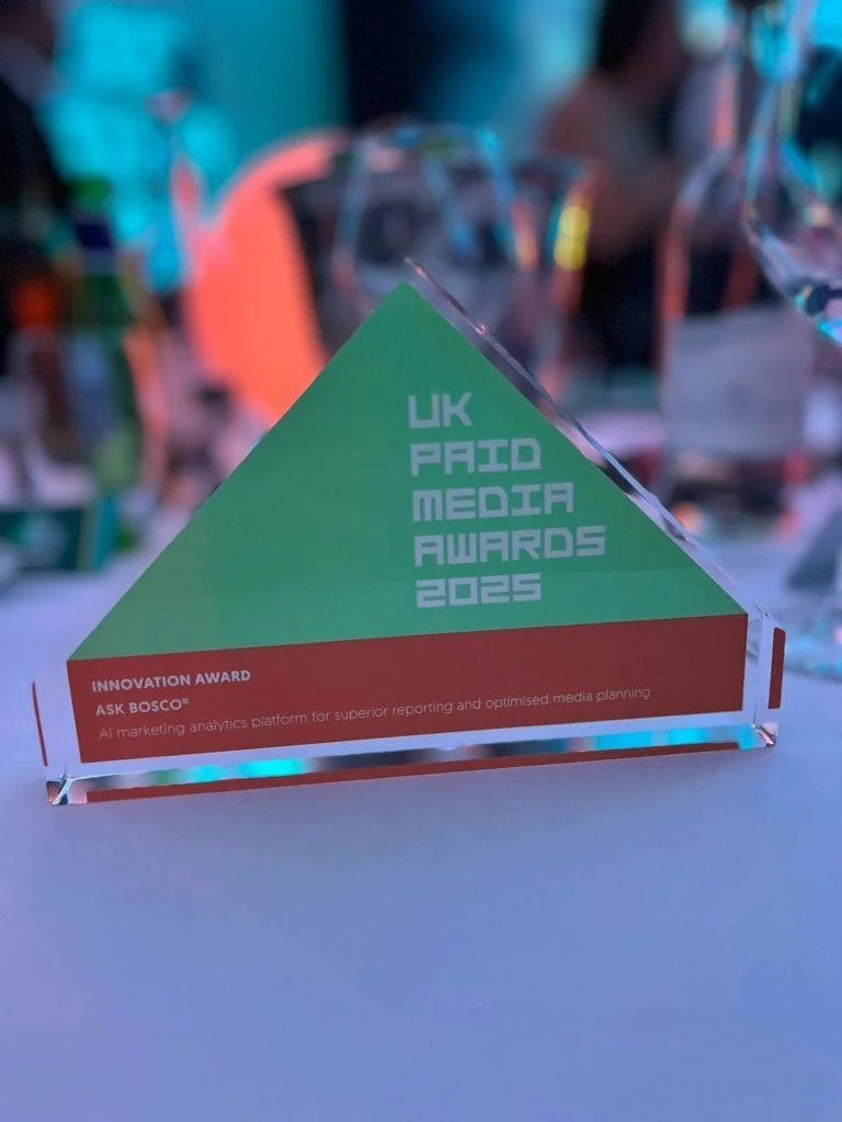 Triangular glass Innovation Award for ASK BOSCO at the UK Paid Media Awards 2025, displayed on a table.