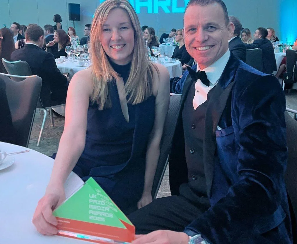 Two smiling attendees at a formal event holding a green UK PRmoment Media Awards 2025 trophy.